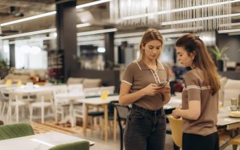 Two Women Discussing While Browsing a Mobile Phone in Modern Furniture Store